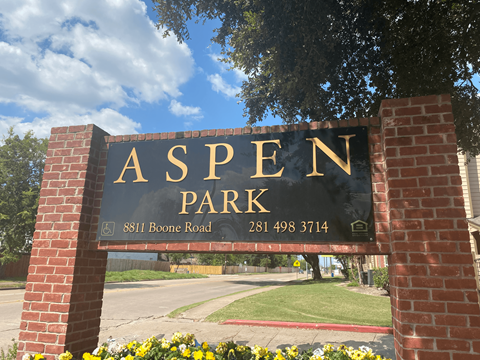 a sign for aspen park in front of a brick sign