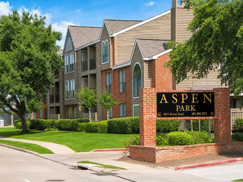 A brick sign that says Aspen Park in front of a building.