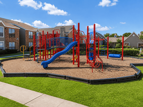A playground with a red and blue slide and a yellow circle on the ground.