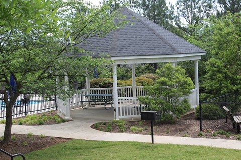 A gazebo with a bench is surrounded by a fence and trees.