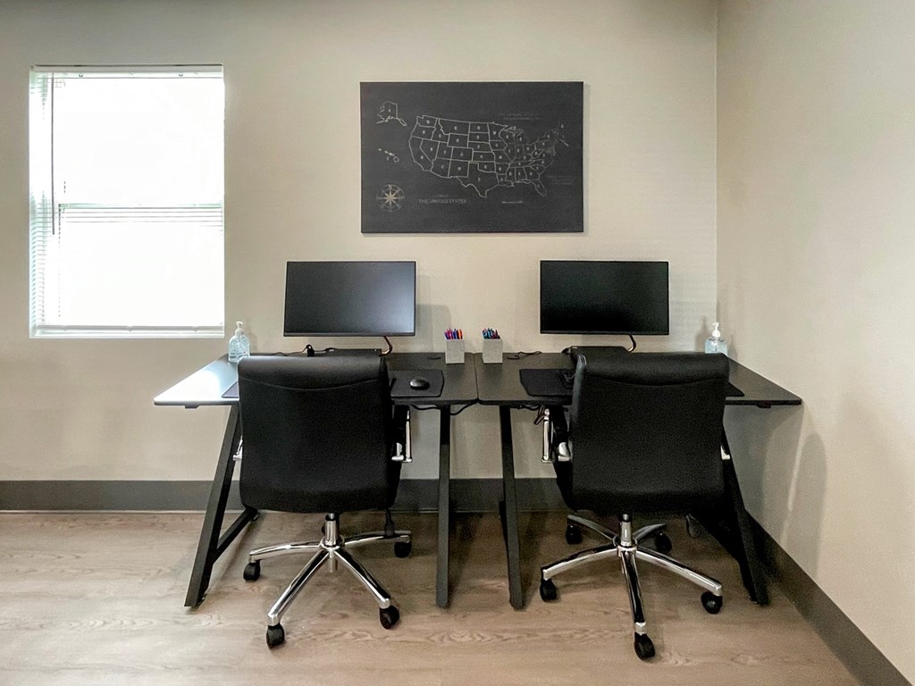 Two black computer desks with chairs and monitors in front of a wall with a map.