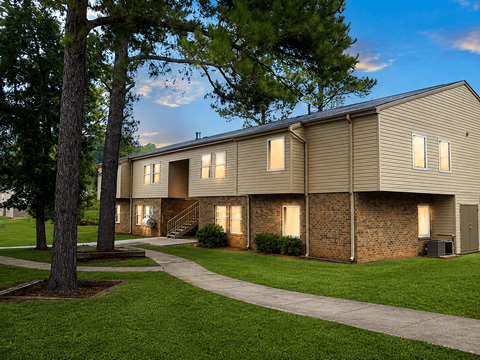 A building with a brown siding and a brick wall is surrounded by a grassy area and trees.