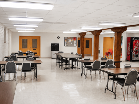 A room with tables and chairs and a TV on the wall.