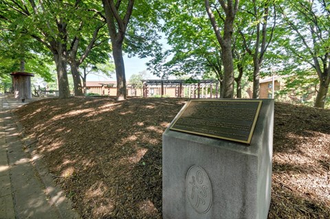 A monument with a plaque on it is surrounded by trees.