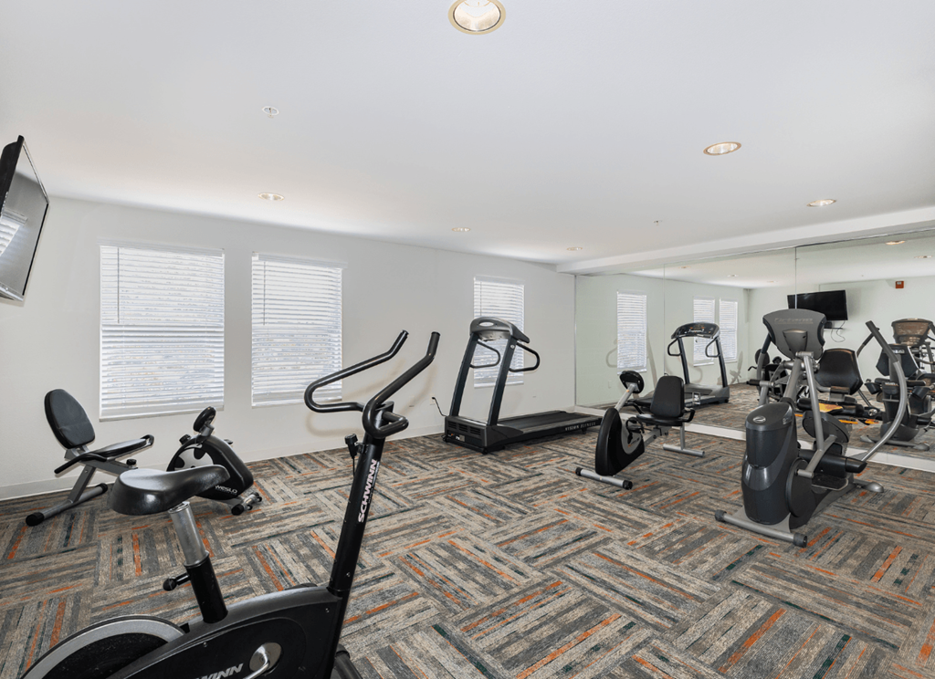 A gym with a variety of exercise equipment including treadmills, stationary bikes, and elliptical machines.