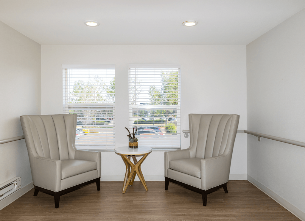 Two chairs and a table are in a room with windows.