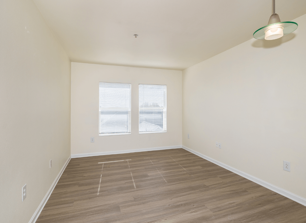 A room with wooden flooring and two windows.