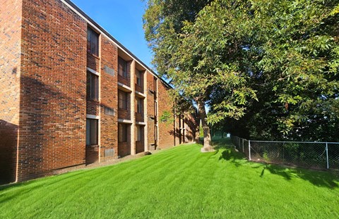 a large brick building with a grass yard and trees