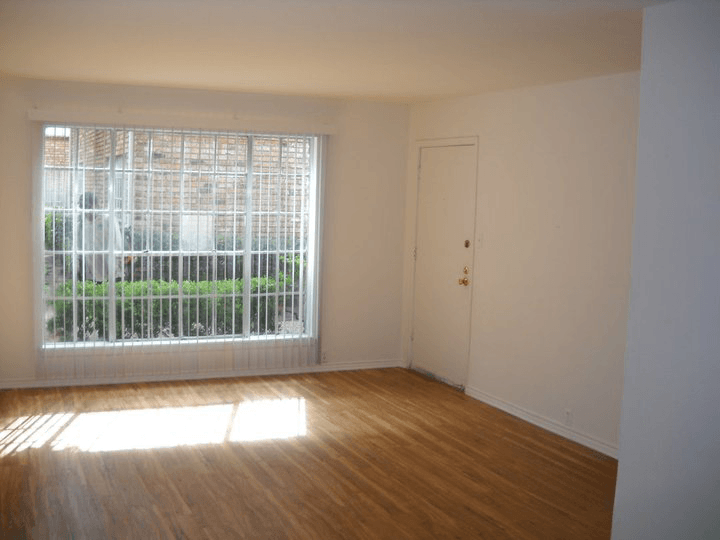 an empty living room with a large window and wooden floors