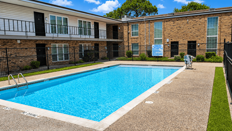 A swimming pool in front of a brick building with a sign that says "For Rent".