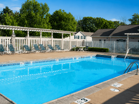 A blue swimming pool with a white fence and trees in the background.