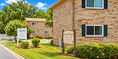 A sign for Desert Winds Apartments stands in front of a brick building.
