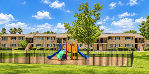 A playground with a slide and a tree in front of a building.