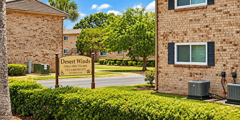 A sign for Desert Winds Apartments stands in front of a brick building.