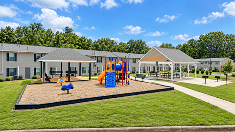 A playground area with a slide and sandbox in front of a building.
