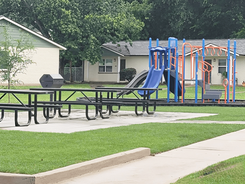 A playground with a blue slide and picnic tables.