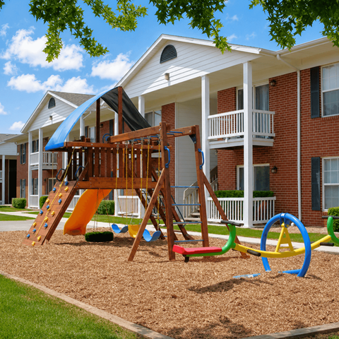A playground with a slide and a wooden swing set in front of a brick apartment building.
