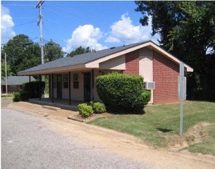 a small brick building with a porch and a road in front of it