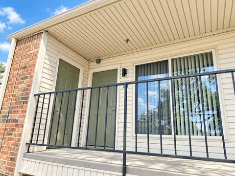 A balcony with a black railing and a window with a view of trees.