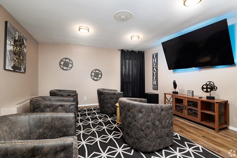 A living room with a large grey chair in the center and a flat screen TV mounted on the wall.