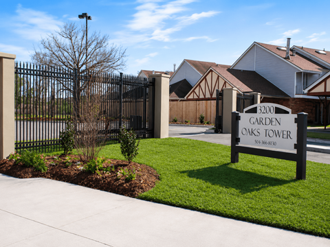 A sign for Garden Oaks Tower is in front of a black gate.