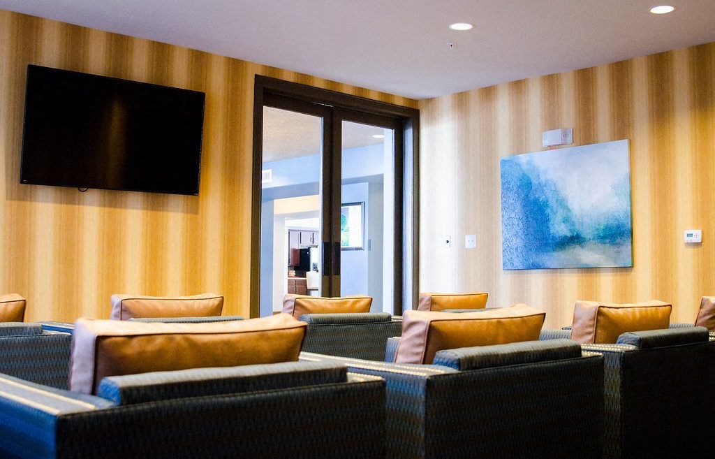 A room with a television, a painting, and several chairs.