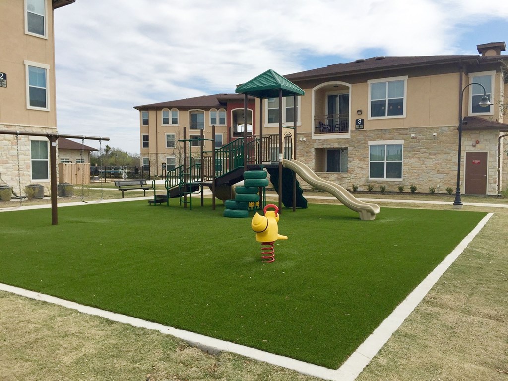 A playground with a yellow duck slide in front of a building.