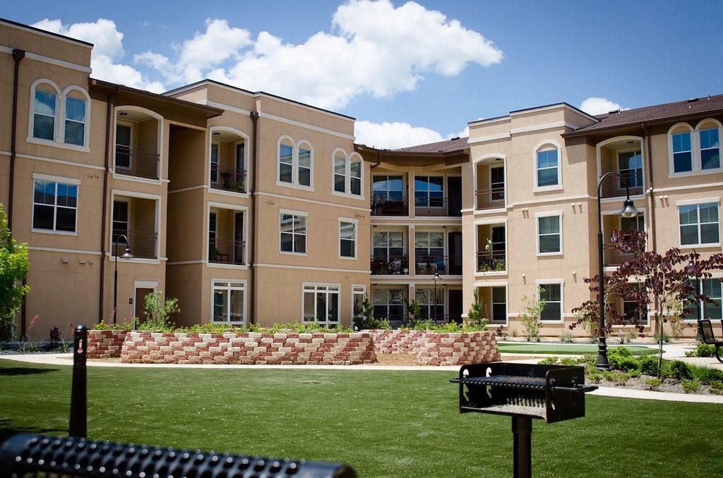 A black mailbox sits in front of a brick wall and a building.
