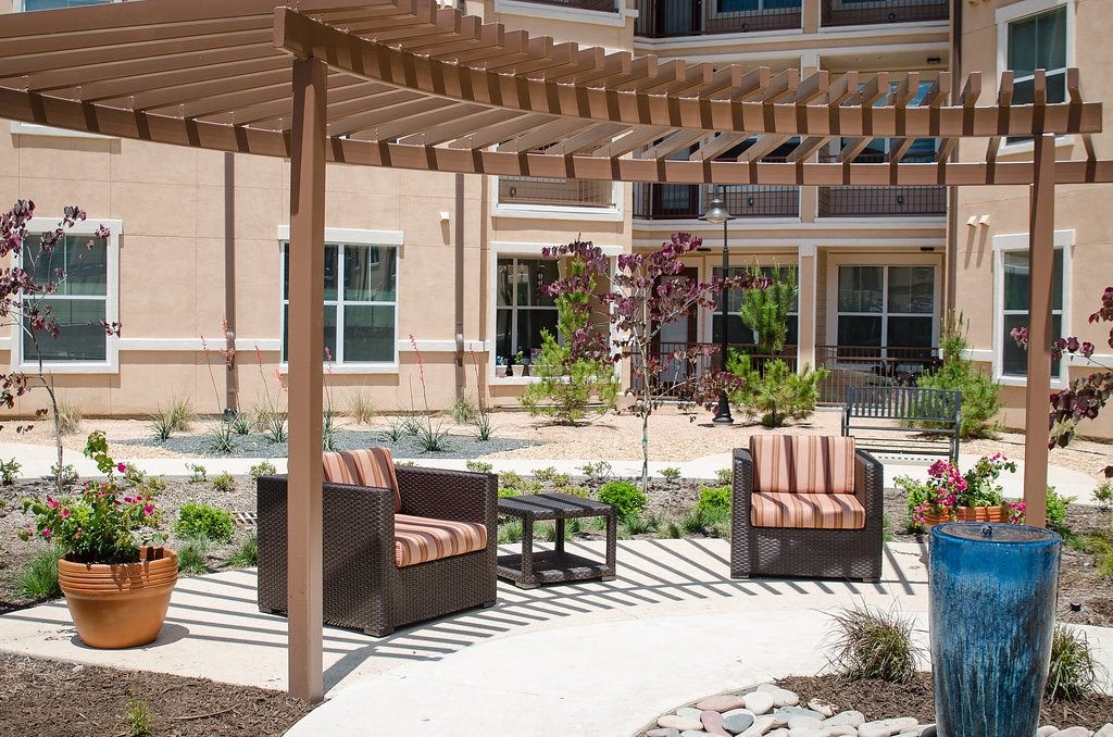 A patio with a wooden pergola and wicker chairs.