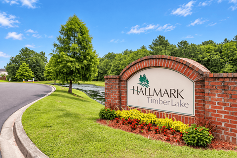 A sign for Hallmark Timber Lake is shown in front of a brick wall and greenery.