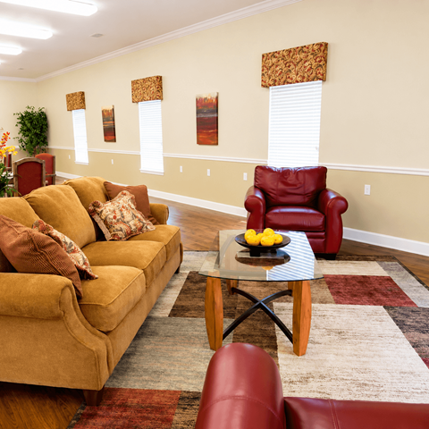 A living room with a yellow couch, a red chair, and a glass coffee table.