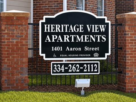 A sign for Heritage View Apartments is displayed in front of a brick wall.