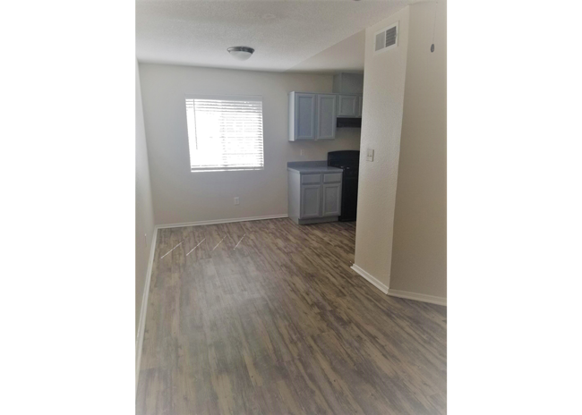 an empty living room with wood floors and a kitchen