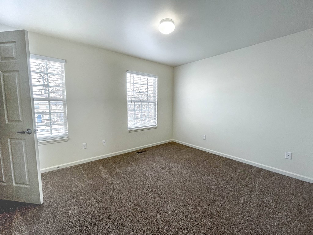 an empty room with carpet and two windows