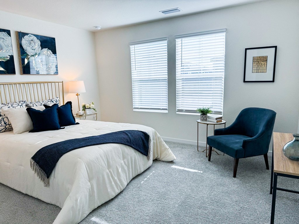 a bedroom with a bed and a chair and two windows