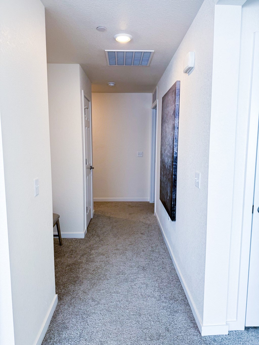 a hallway with white walls and a carpeted floor and a white ceiling fan