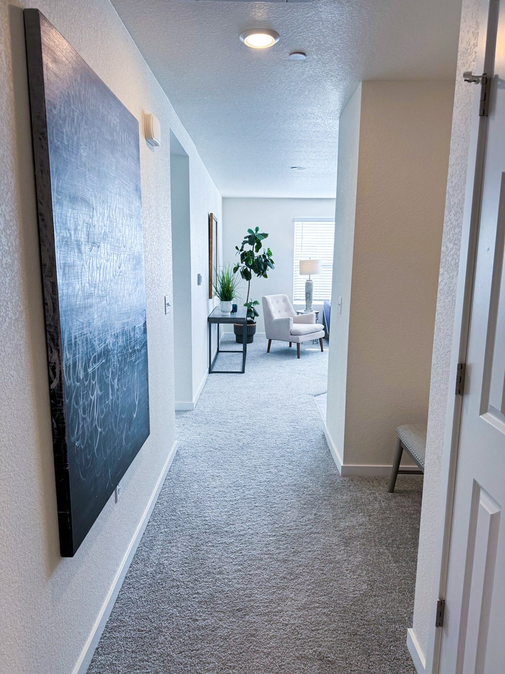a hallway leading to a living room with a blue painting on the wall