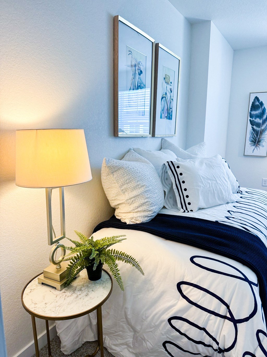 a bedroom with a bed and a table with a lamp and pictures on the wall