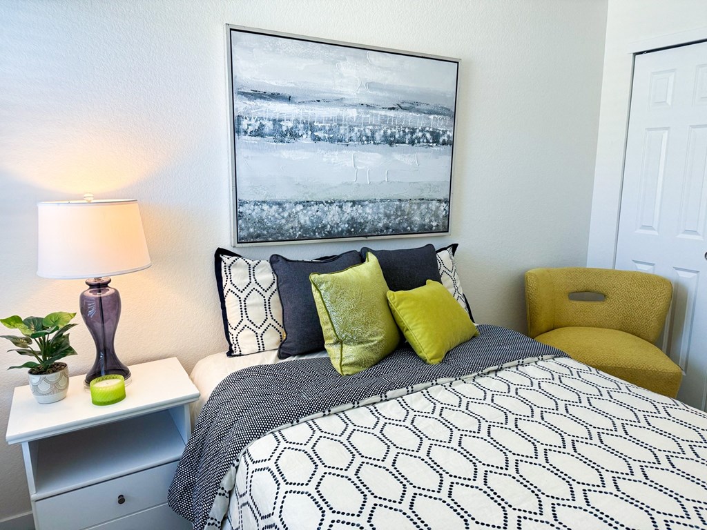 a bedroom with a bed and a yellow chair and a white and black bedspread