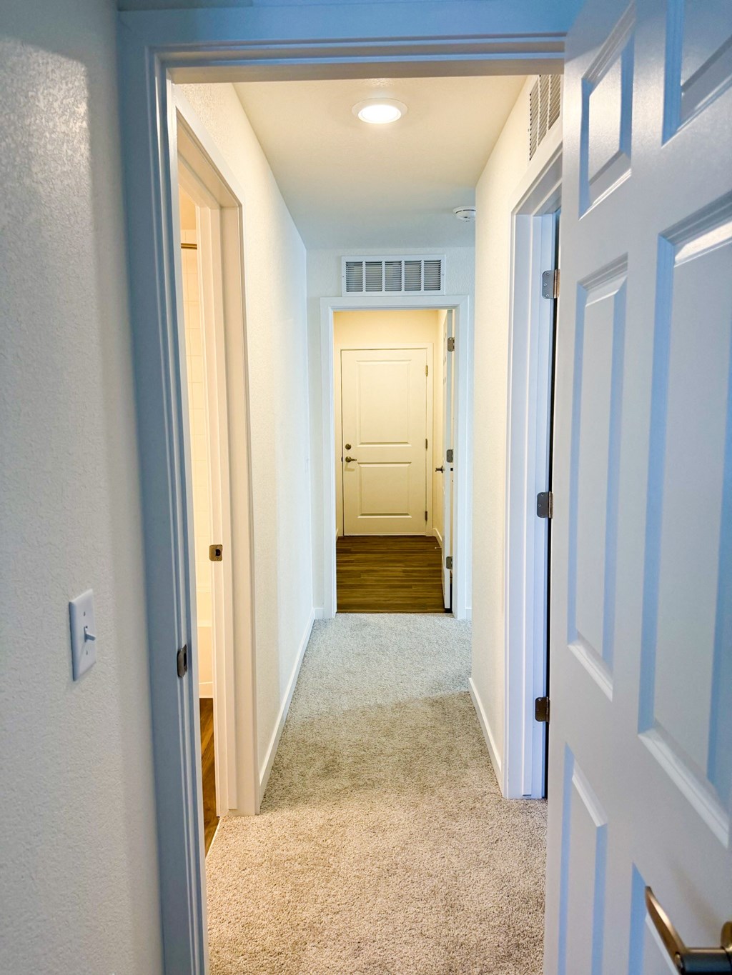 a hallway with a carpeted floor and white walls and a white door