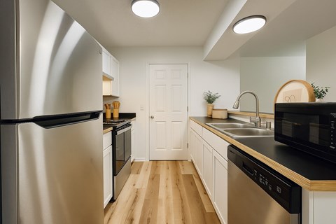 A modern kitchen with a stainless steel refrigerator and wooden flooring.