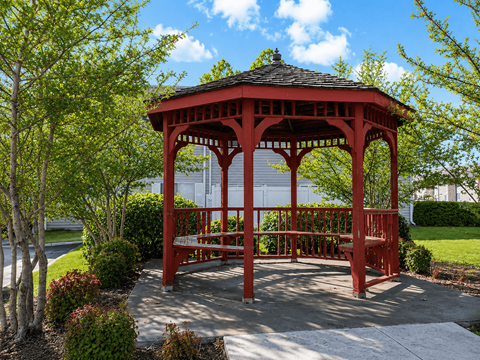 A red gazebo is surrounded by trees and bushes.