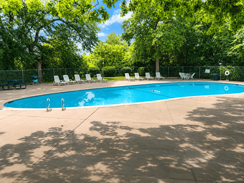 A swimming pool surrounded by trees and chairs.