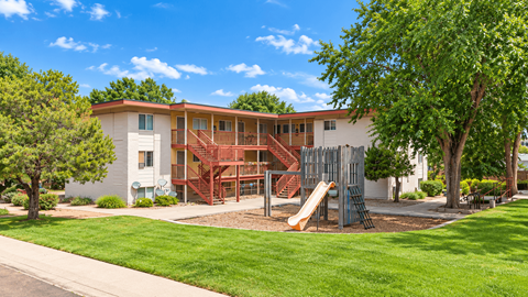 A playground with a slide is in front of a two-story building.