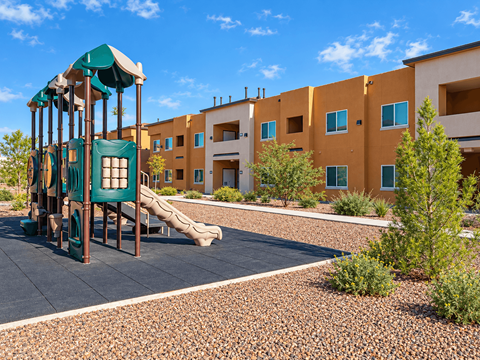 A playground with a green slide and a brown and yellow building in the background.