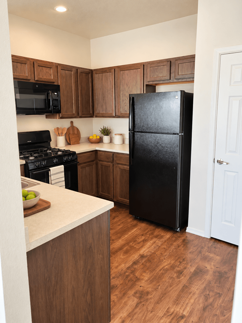 A black refrigerator stands in a kitchen with wooden cabinets and a white door.