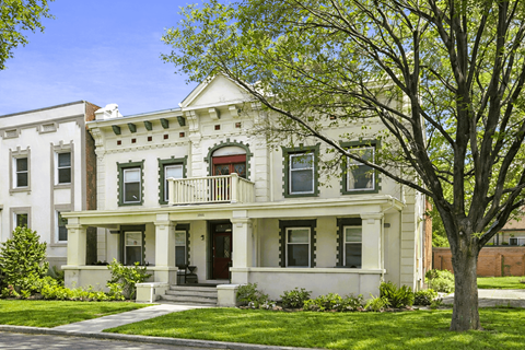 A white two-story house with a red door and a balcony.