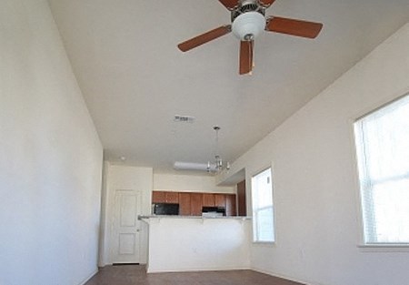 an empty living room with a ceiling fan and a kitchen