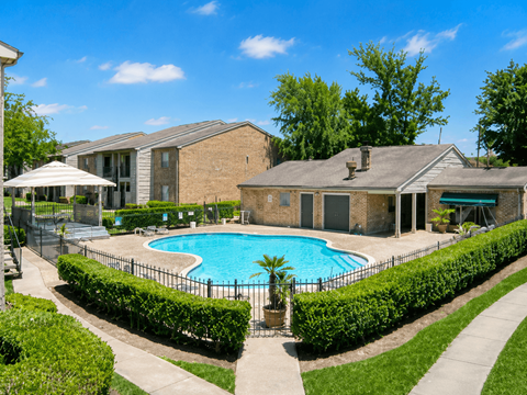 A pool surrounded by a black fence and green bushes.