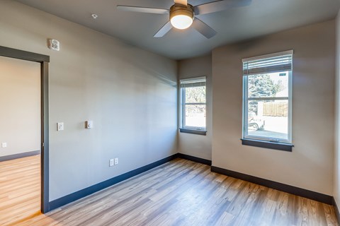 A room with a ceiling fan and two windows.